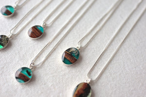 blue and wood resin pendants in sterling silver frames sit on a canvas background