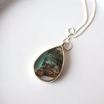Load image into Gallery viewer, sterling silver teardrop frame encases a fragment of birch bark in softly tinted resin. The necklace sits on a white ceramic background. 

